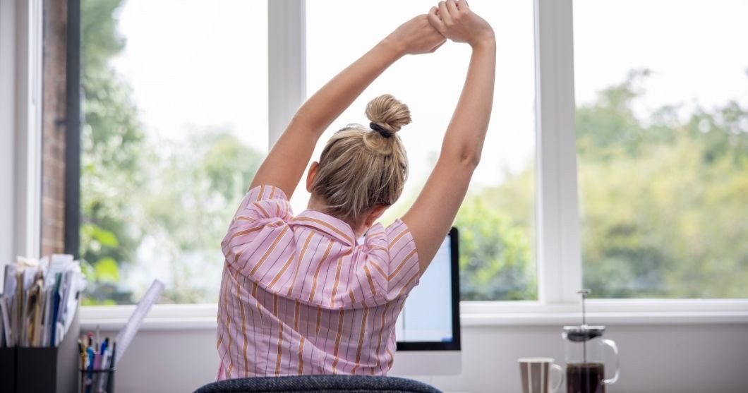 Photo d'une femme s'étirant les bras devant son écran d'ordinateur